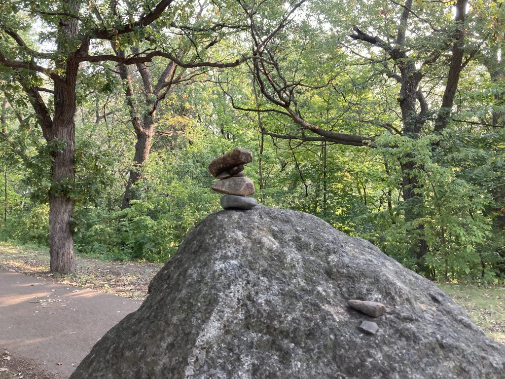 a big boulder with several small stones stacked on it. The top stone, much bigger than the one just beneath it.