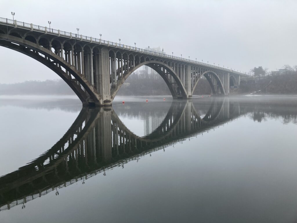 an arched bridge stretching from one end of the frame to the other with a clear reflection on the river surface